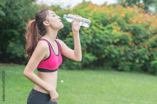 young attractive woman drinking water from plastic bottle in the park