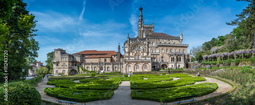 BUSSACO, PORTUGAL - 27 APRIL 2014: A panorama showing visitors enjoying the facade and gardens of the luxury hotel at Bussaco Palace near Luso in Portugal on a sunny summer's day.