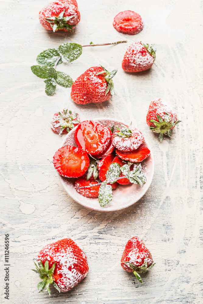Bowl with sliced strawberries sprinkle with powdered sugar on white wooden background, top view