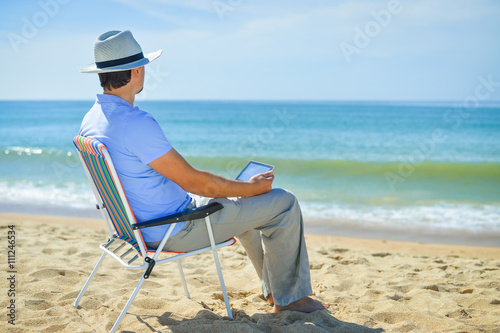 Man using tablet relaxing on ocean beach  blue sky outdoors background