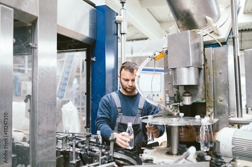 Serious manual worker doing his job on factory production line for water purification and bottling.