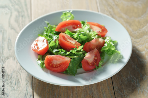 fresh summer salad with tomatoes, rucola and frillis leaves in plate on wood table, shallow focus