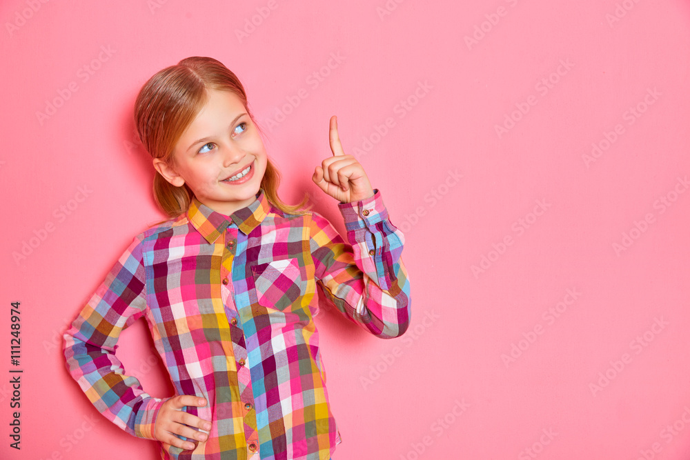 Pretty little girl standing on pink background with raised finger up. Copy space. Pretty little girl standing on pink background with raised finger up. Copy space.