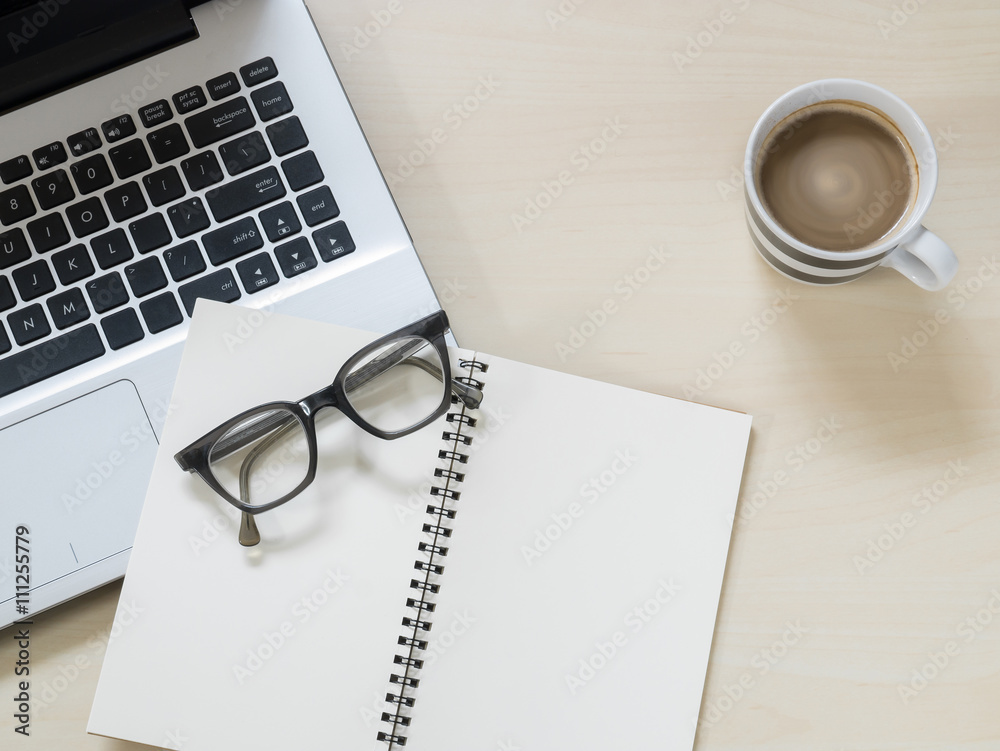 Eyeglasses on notebook, laptop computer and a cup of hot coffee on wooden table Eyeglasses on notebook, laptop computer and a cup of hot coffee on wooden table