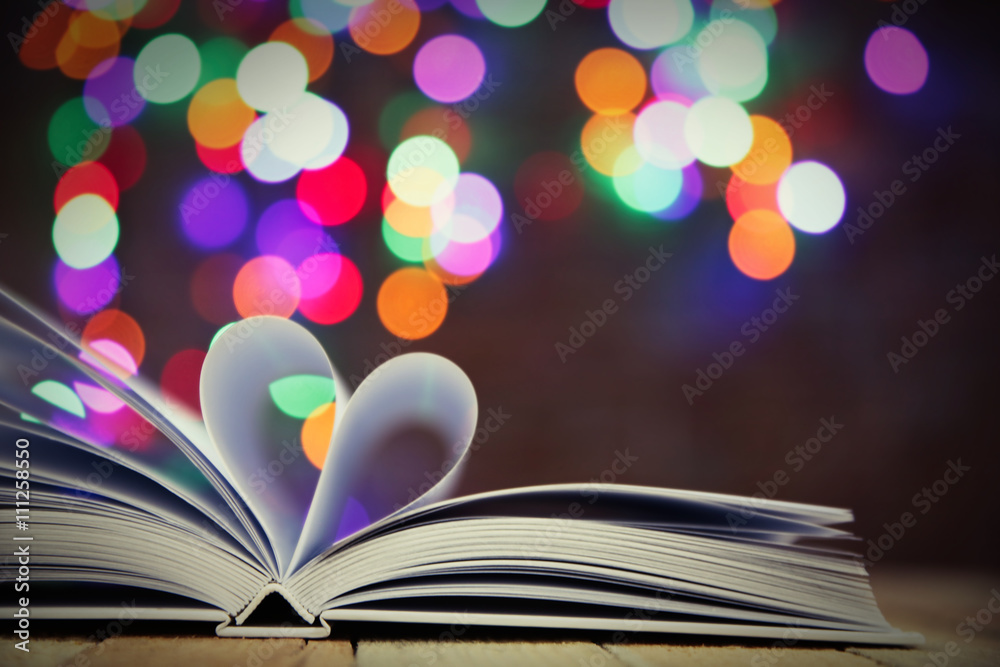 Sheets of book curved into heart shape on wooden table against unfocused lights Sheets of book curved into heart shape on wooden table against unfocused lights