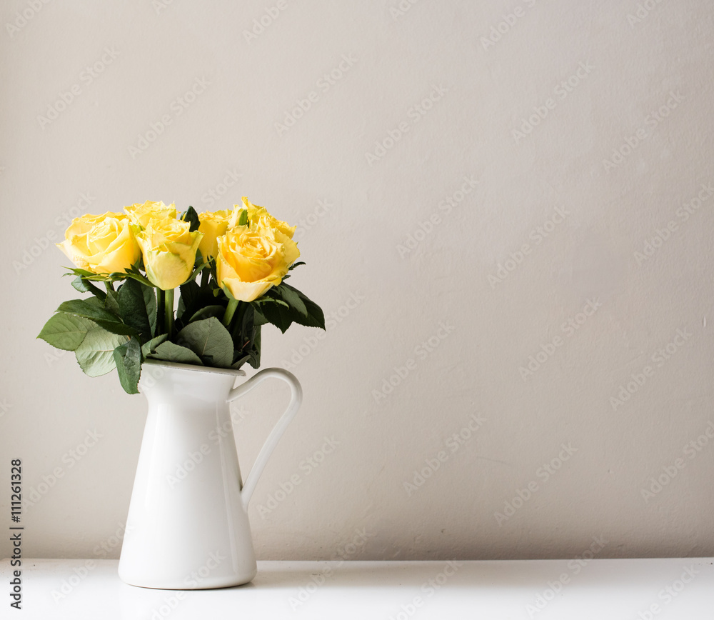 Obraz premium Yellow roses in white jug on white table against neutral background