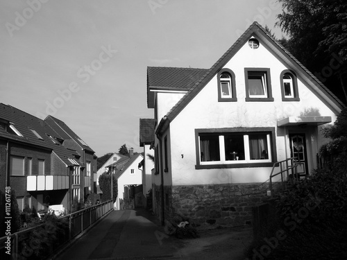 Straße mit altem Wohnhaus mit Dachgaube und Spitzgiebel im Sonnenschein in Oerlinghausen bei Bielefeld am Hermannsweg im Teutoburger Wald in Ostwestfalen Lippe, fotografiert in klassischem Schwarzweiß photo