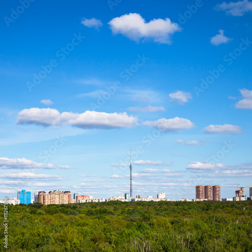 white clouds in blue sky over town and green woods