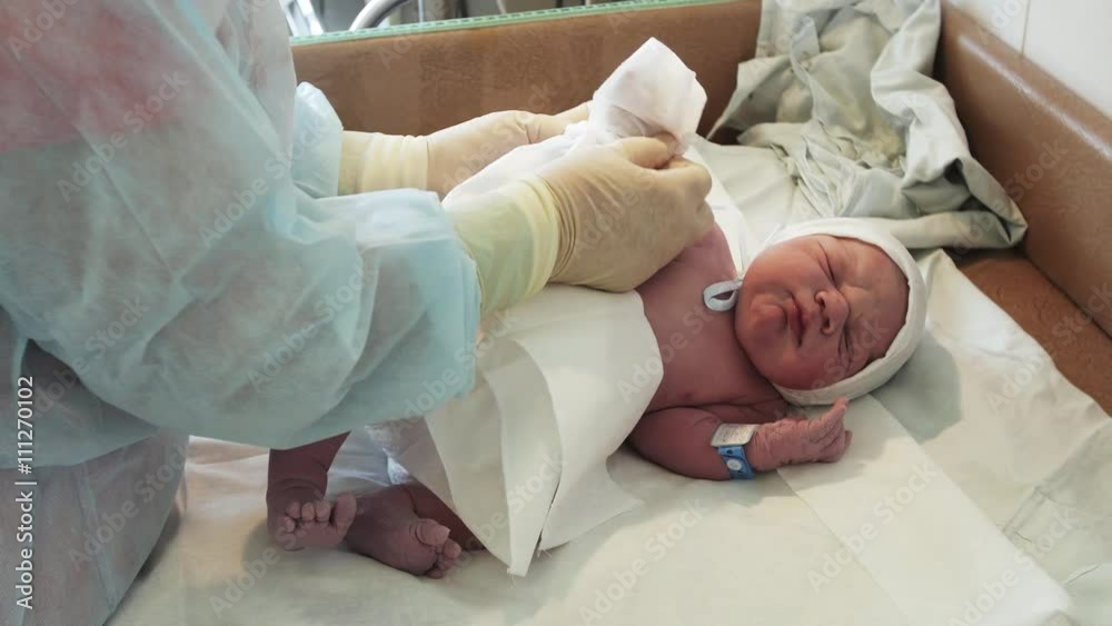 Nurse put on white disposable diaper on newborn crying baby in diapers