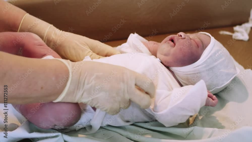 Nurse put on white disposable diaper on newborn crying baby in hat after birth. Maternity hospital. Nurse put on white disposable diaper on newborn crying baby in hat after birth. Maternity hospital.