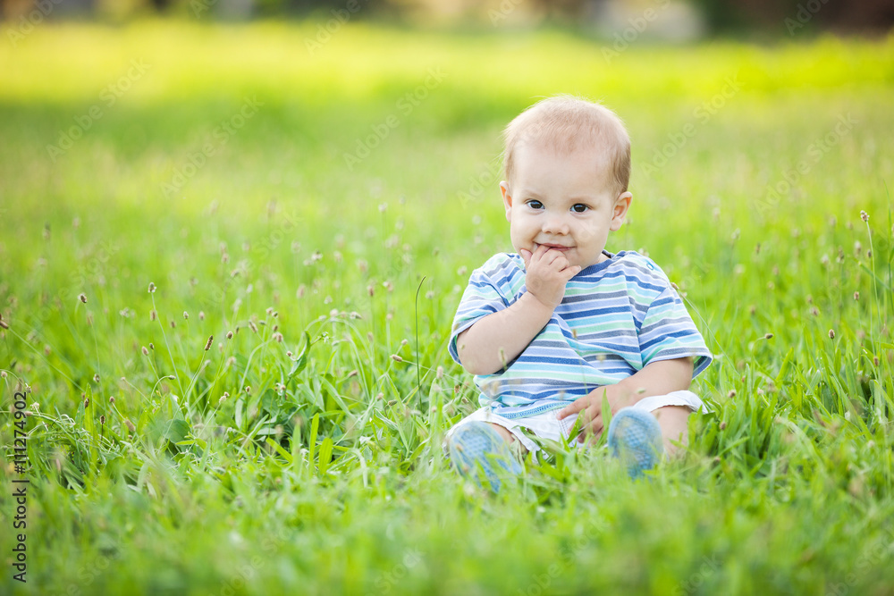 Happy small boy sitting on green grass in a park Happy small boy sitting on green grass in a park