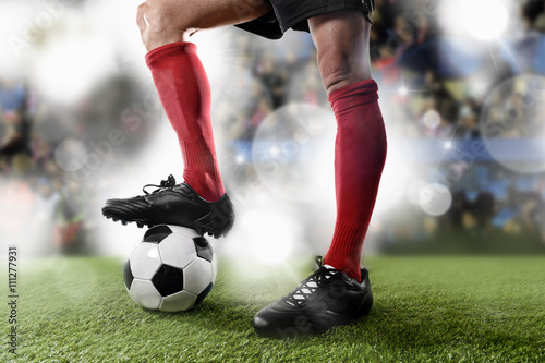 football player in red socks and black shoes plaing with the ball standing on stadium pitch