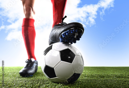 close up legs feet football player in red shocks and black shoes posing with ball standing on grass outdoors