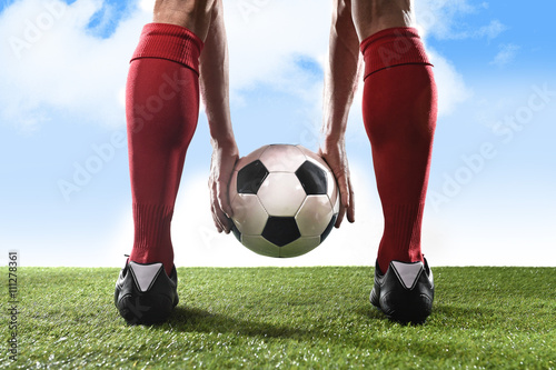 football player in red socks and black shoes holding ball in his hands placing free kick or penalty