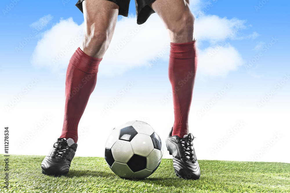 legs of football player in red socks and black shoes running and dribbling with ball playing outdoors