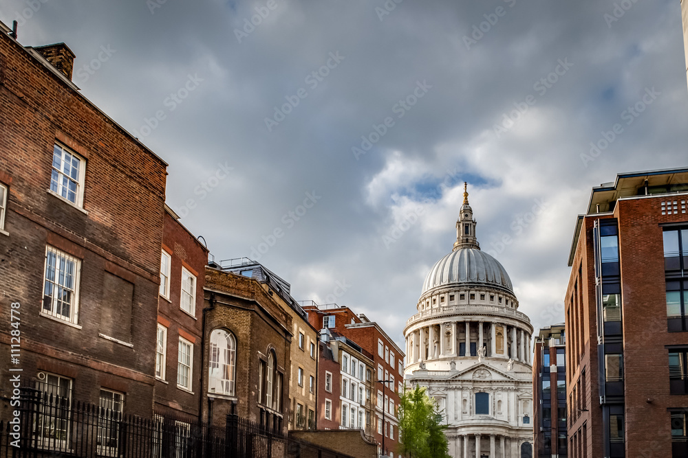 St Paul’s cathedral seen from a narrow alley enclosed by brick buildings on a cloudy day in summer