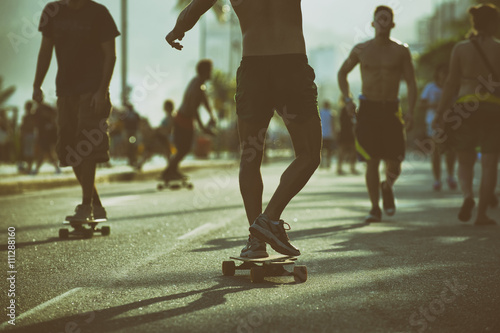Brazilian skaters skate along the Ipanema Beach beachfront road in a toned scene in Rio de Janeiro, Brazil