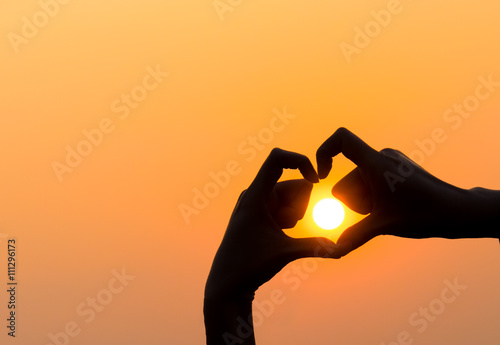 Woman's hands forming a heart shape with sunset silhouette