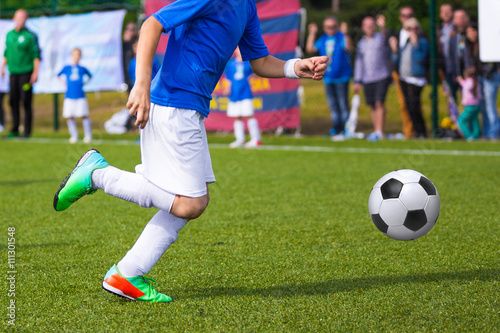 Young soccer player kicking ball in sports blue outfit. Boy kicking soccer ball on sports field. Soccer football training session for children, teens