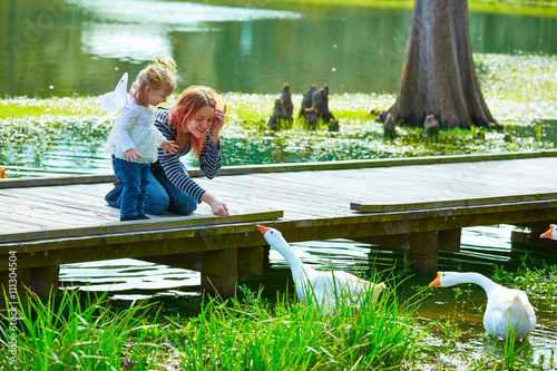 Kid girl and mother playing with ducks in lake photo