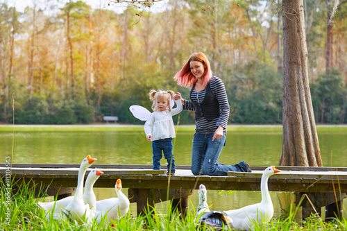 Kid girl and mother playing with ducks in lake photo