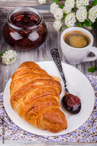 Closeup freshly baked  croissant with strawberry jam and coffee cup  on vintage rustic tray. Breakfast concept.