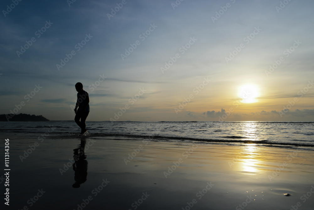 Fototapeta premium Silhouette of a Boy Walking on the beach at sunset backdrop.