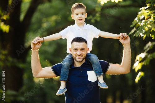 happy little boy stretching out hands while his father carrying him on shoulders