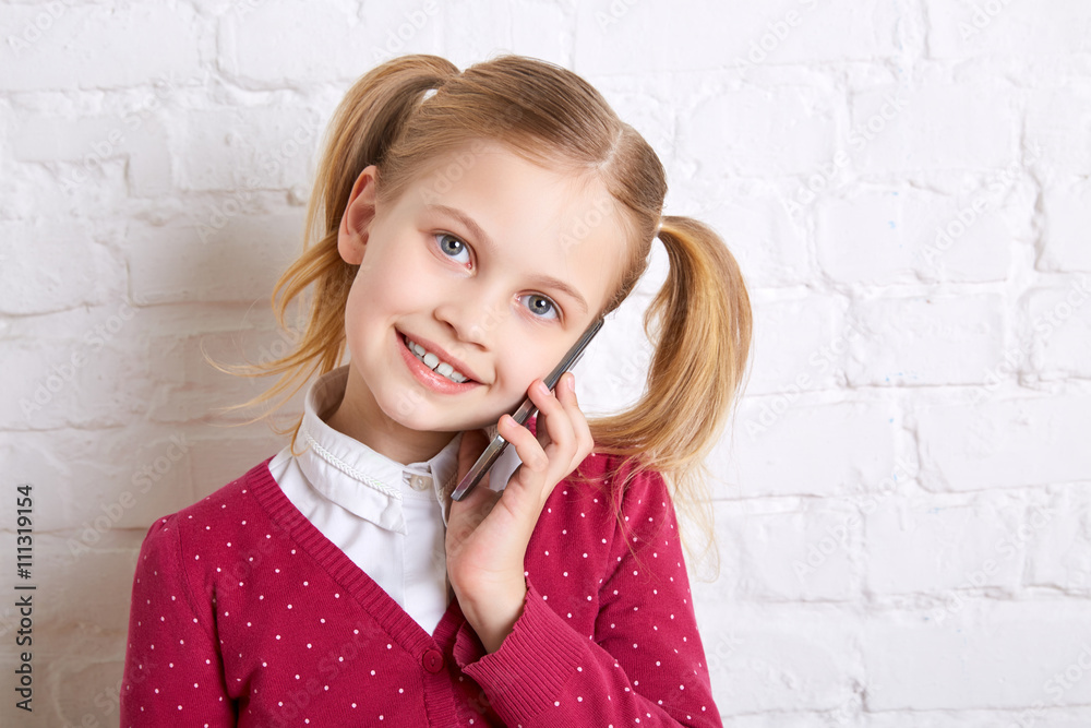 Pretty little girl standing on light background holding and talking a phone.