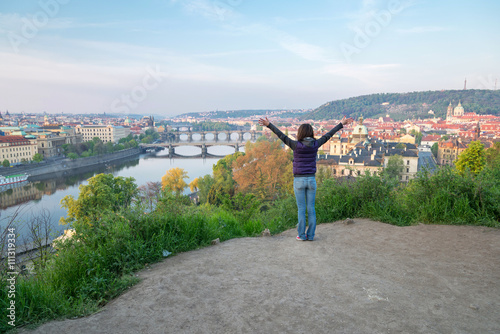 young woman with hands up on the hill over Vltava river and brid