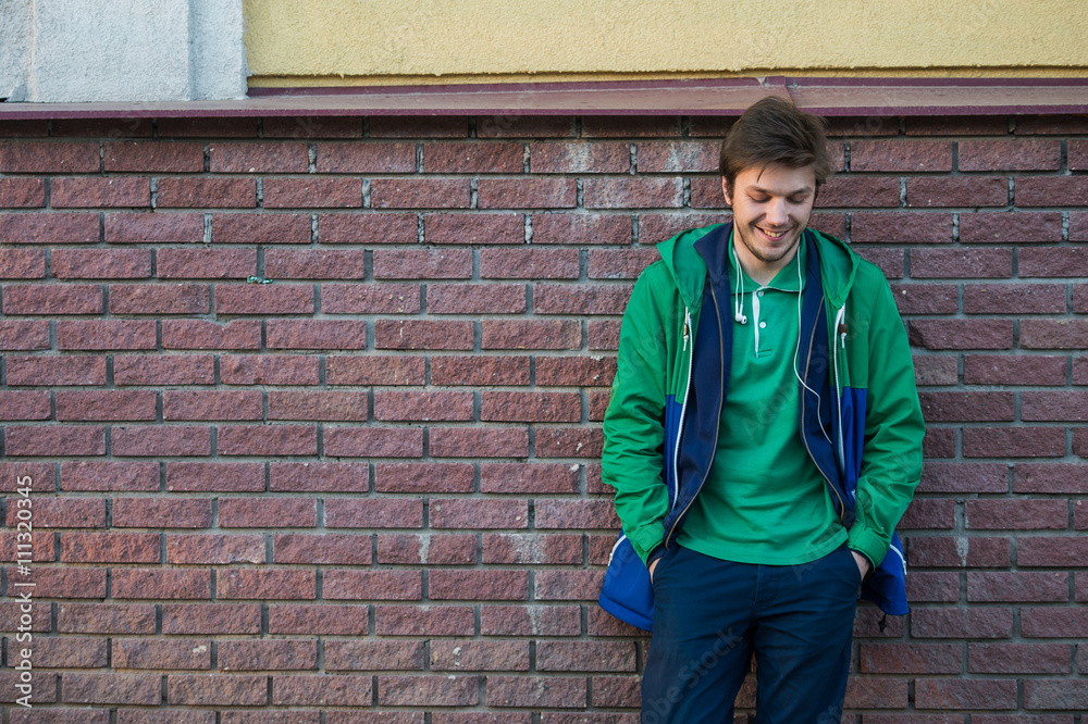 Common young man wearing green t-shirt jacket and jeans against a red brick wall looking to the camera Common young man wearing green t-shirt jacket and jeans against a red brick wall looking to the camera