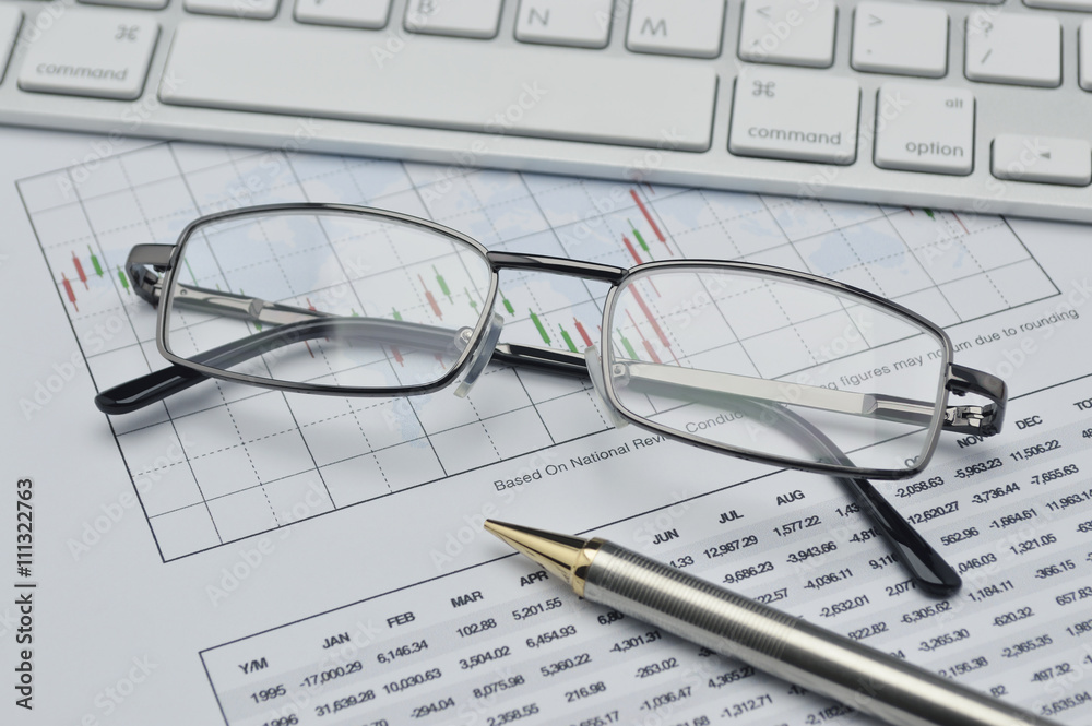 Glasses, pencil and keyboard on stock market graph, financial co Glasses, pencil and keyboard on stock market graph, financial co