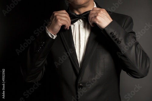 Fotografie Close-up of  gentleman wearing black tie straightens his bowtie.