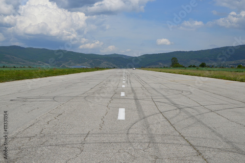 Reaching the horizon straight old tarmac runway with a car in the distance