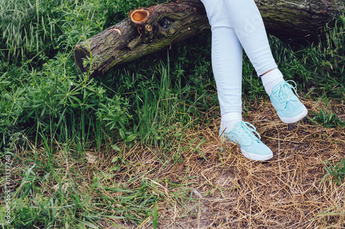 Female feet in sneakers and jeans on a log in the forest