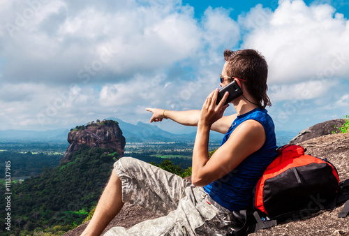 Man with mobile phone on the top and shows up the mountain