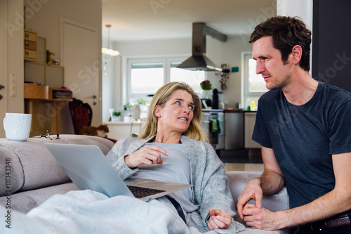 Joyful couple relax and work on laptop computer at modern living room at home. Both discuss some options