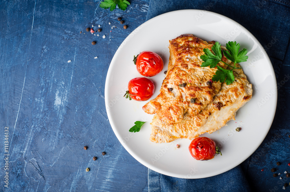 Roasted turkey steak with tomatoes, parsley and spice in white bowl on dark blue background. Selective focus. Toned image Roasted turkey steak with tomatoes, parsley and spice in white bowl on dark blue background. Selective focus. Toned image