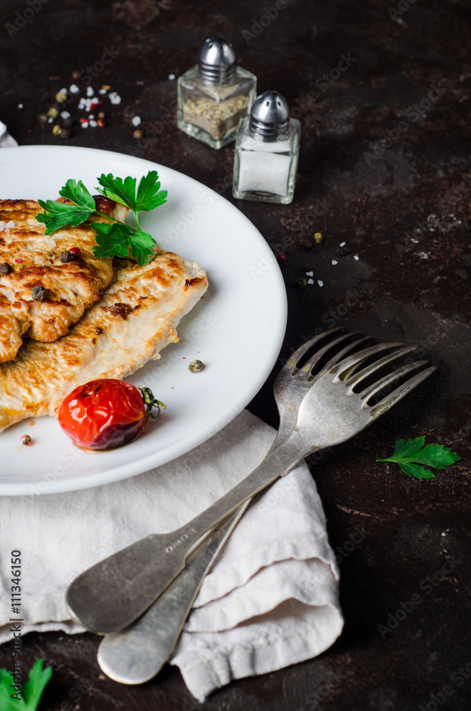Roasted turkey steak with tomatoes, parsley and spice in white bowl on dark slate background. Selective focus. Toned image Roasted turkey steak with tomatoes, parsley and spice in white bowl on dark slate background. Selective focus. Toned image