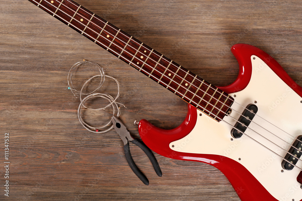 Fototapeta premium Electric guitar with pliers and strings on wooden background