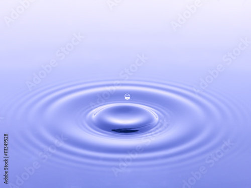 single water drop falling into blue water
