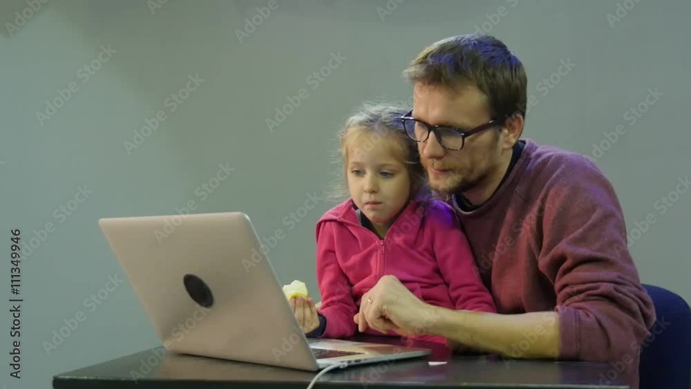 Kid is Eating Father Clicks a Laptop Girl and Dad Talking to a Kid Teaches His Daughter to Work With Laptop Pointing Man and Kid Are Sitting at the Table Kid is Eating Father Clicks a Laptop Girl and Dad Talking to a Kid Teaches His Daughter to Work With Laptop Pointing Man and Kid Are Sitting at the Table