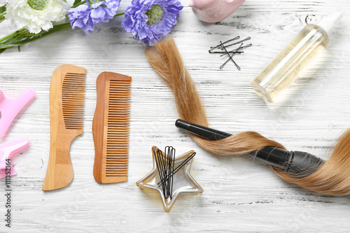 Fototapeta Naklejka Na Ścianę i Meble -  Strand of hair with flowers, barber equipment and tools on light wooden background