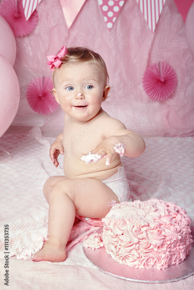 Portrait of cute adorable Caucasian baby girl with blue eyes in pink tutu skirt celebrating her first birthday with gourmet cake and balloons looking away, cake smash first year concept