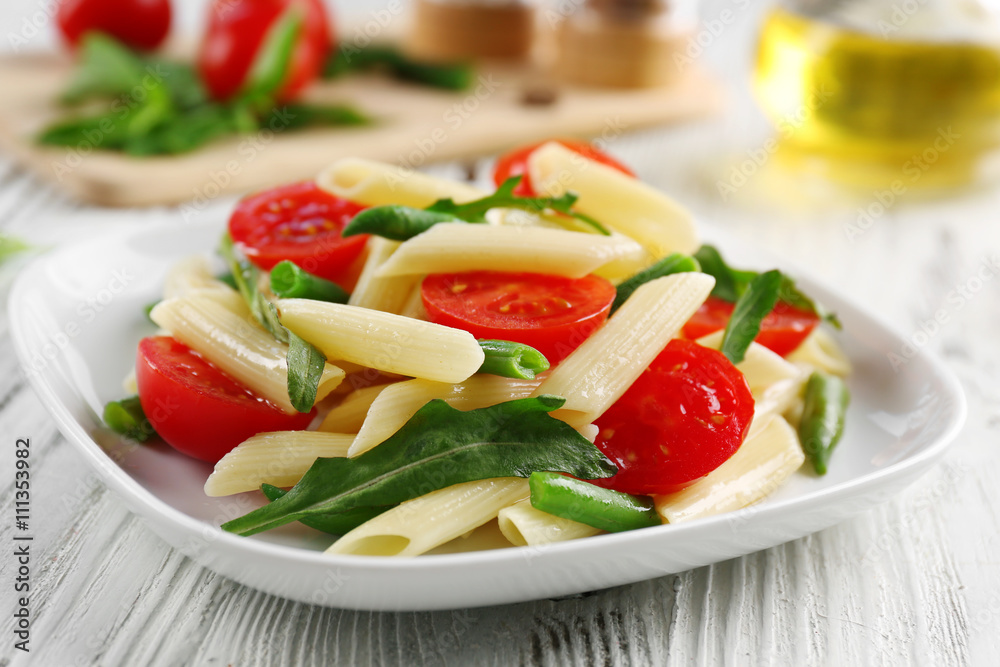 Boiled penne pasta with tomatoes, French bean and arugula on white plate Boiled penne pasta with tomatoes, French bean and arugula on white plate