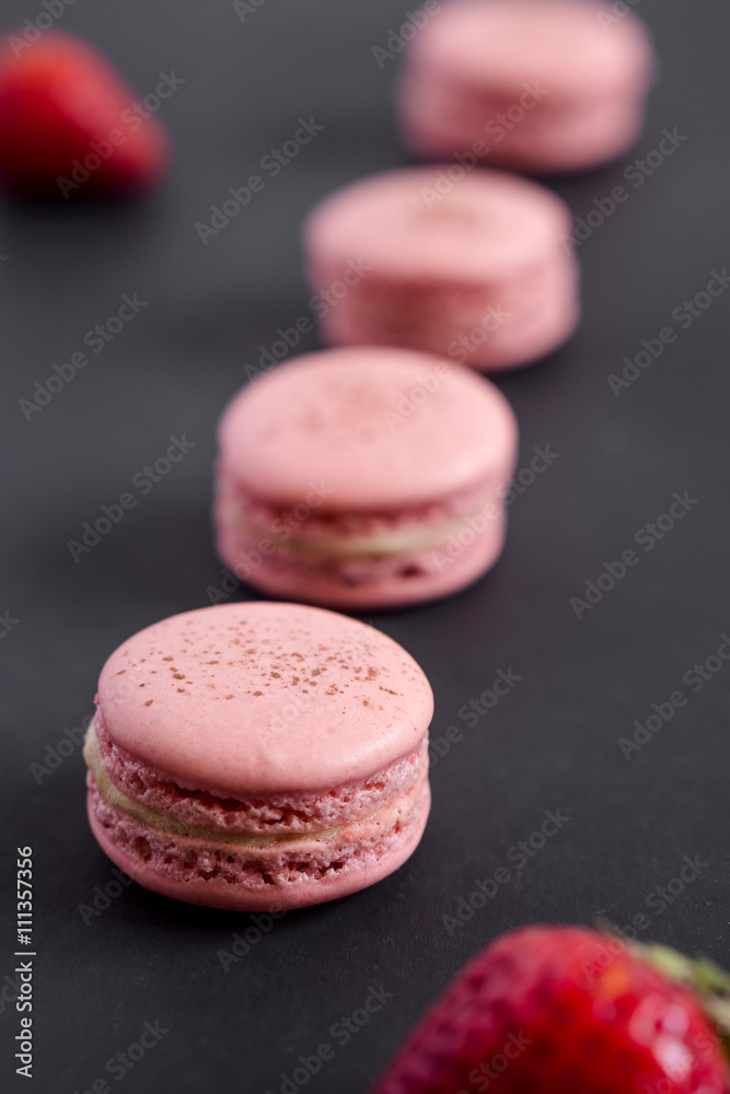 Strawberry macarons on a dark background. These delicate french pastries are made of two meringue cookies and a sweet filling in the center. Light & crisp, these are the perfect luxurious dessert. Strawberry macarons on a dark background. These delicate french pastries are made of two meringue cookies and a sweet filling in the center. Light & crisp, these are the perfect luxurious dessert.
