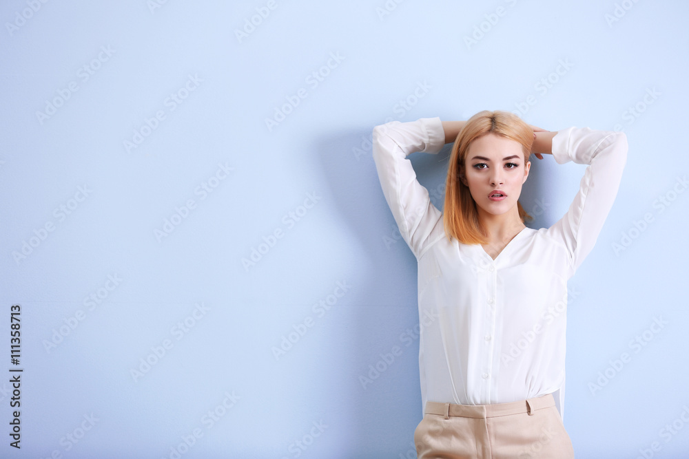 Beautiful blonde young woman in white shirt and beige pants on blue wall background Beautiful blonde young woman in white shirt and beige pants on blue wall background