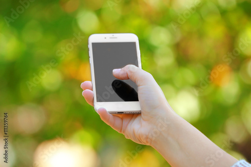 A female hand holding a mobile phone outdoors, on blurred background