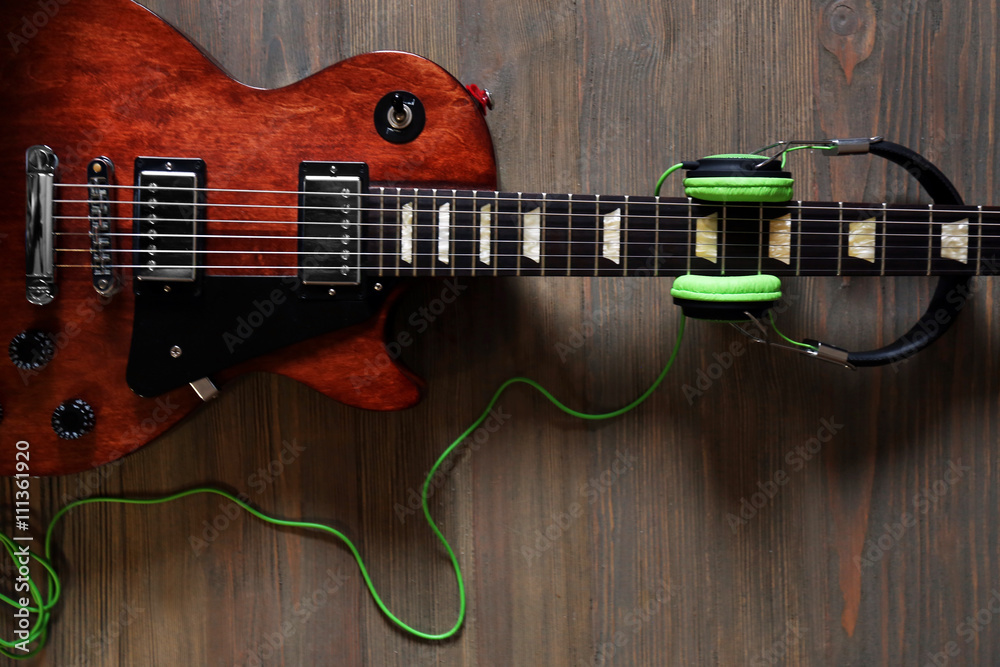 Naklejka premium Brown electric guitar with headphones on wooden background
