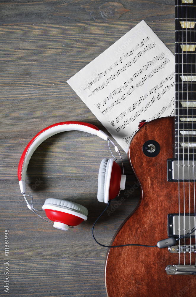 Fototapeta premium Brown electric guitar with headphones and notes on wooden background